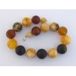 A three colour amber necklace, composed of large graduated spherical beads, individually knotted, on