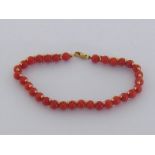 A coral bead bracelet, composed of a line of uniform 5.3mm beads, accented by two rows of gold