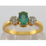 An emerald and diamond ring, the central oval cut stone 6 x 3.9mm, flanked by two diamond