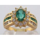 An emerald and diamond ring, the central oval cut emerald approx. 0.43 carat, in a surround of