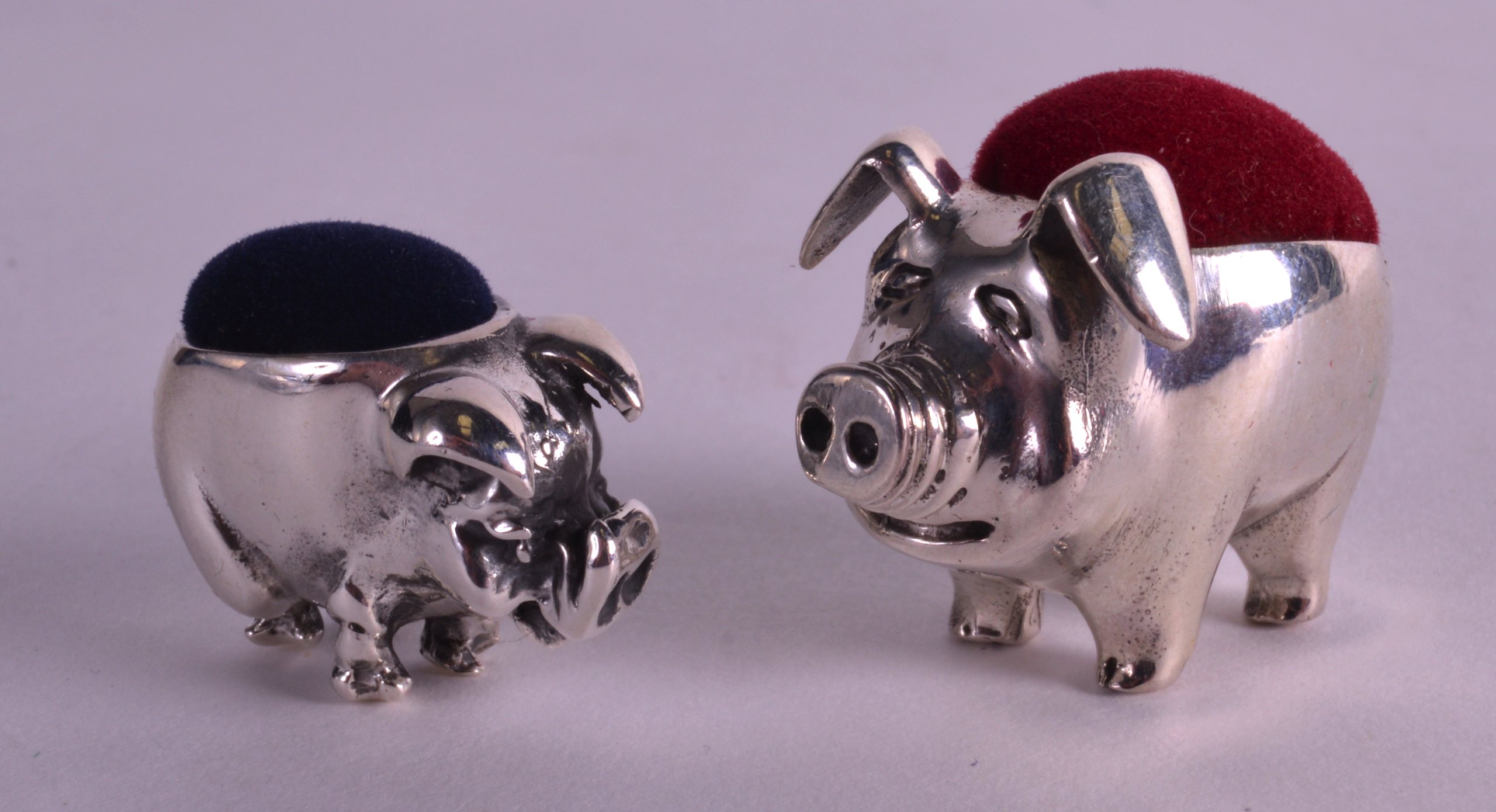 A PAIR OF STERLING SILVER PIG PIN CUSHIONS.