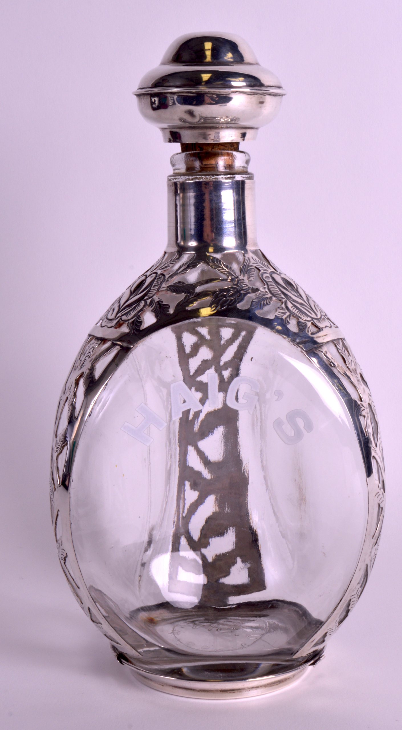 A MEXICAN SILVER OVERLAID 'HAIGS' WHISKEY DECANTER AND STOPPER decorated with foliage. 10.75ins