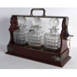 AN EARLY 20TH CENTURY CARVED MAHOGANY THREE BOTTLE TANTALUS one with silver plated decanter label.