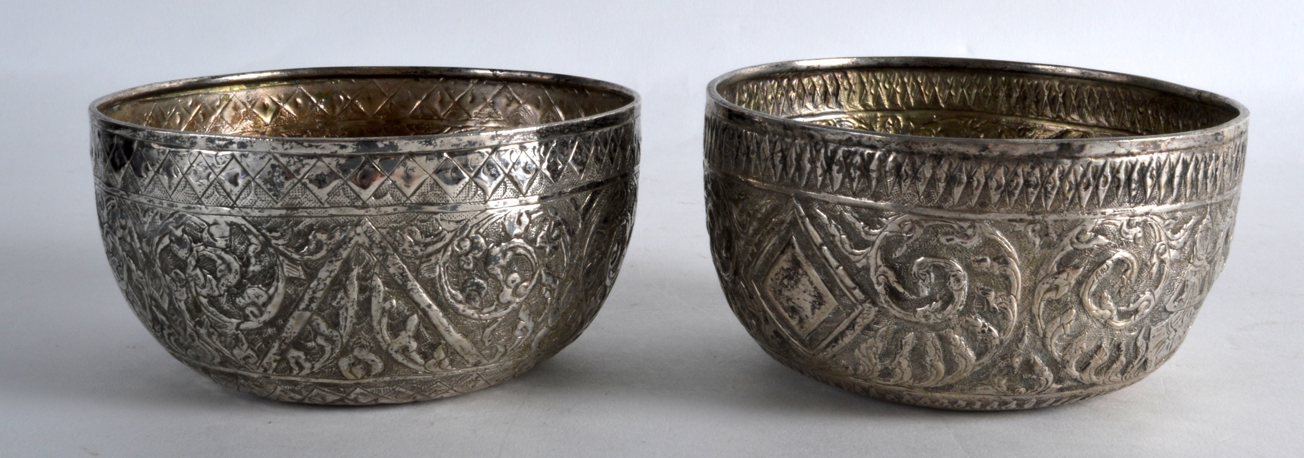 A PAIR OF 19TH CENTURY INDIAN EMBOSSED SILVER BOWLS decorated with buddhistic figures. 2.5oz. 4.5ins