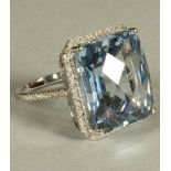 A TOPAZ PLAQUE RING, the emerald cut stone claw set to a border pave set with numerous small