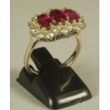 A RUBY AND DIAMOND TRIPLE CLUSTER RING, the three oval cut rubies claw set to a shaped border of