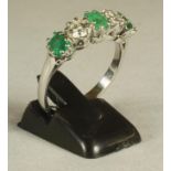 AN EMERALD AND DIAMOND FIVE STONE RING, claw set with three trap cut emeralds and two brilliant