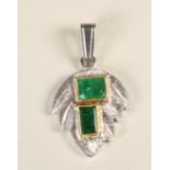 AN EMERALD PENDANT, the two step cut stones open back collet set asymmetrically to a platinum leaf