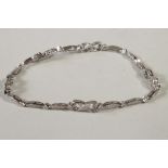 A DIAMOND BRACELET, the thirteen eliptical links interspersed with four open scroll panels all