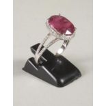 A RUBY AND DIAMOND RING, the oval cut ruby of approximately 5.30cts claw set to a border of pave set