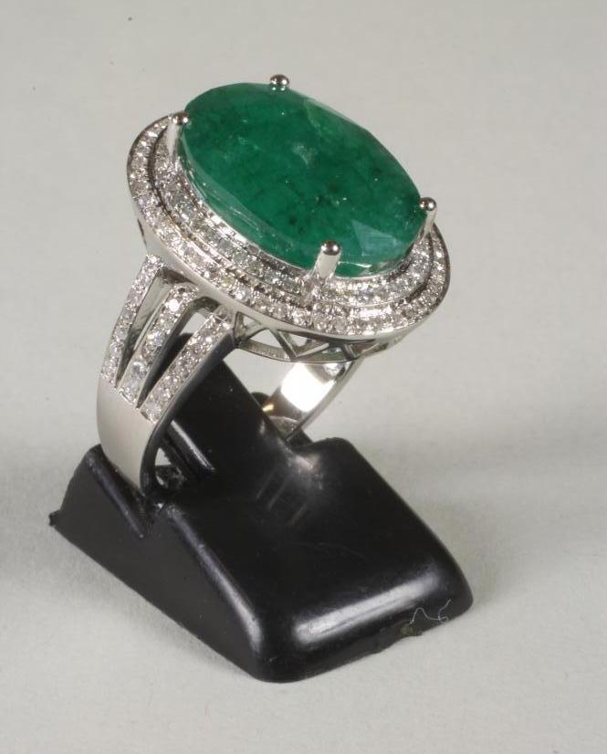 AN EMERALD AND DIAMOND CLUSTER RING, the oval cut emerald of approximately 8cts, claw set to a