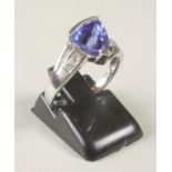 A TANZANITE RING, the triangular cut stone part bezel set to open shoulders each set with two