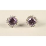 A PAIR OF AMETHYST AND DIAMOND CLUSTER EAR STUDS, the square cut amethysts claw set to a border of