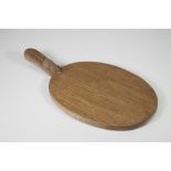 AN OAK CHEESE BOARD by Robert Thompson of plain oval form with carved mouse trademark to handle, 16"