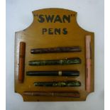 A "Swan Pens" wood easel display stand with seven fountain pen outers, 9 1/4" x 7 3/4"