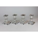 A set of four silver plated dwarf candlesticks with embossed floral scroll borders on scalloped