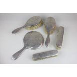 A George V silver backed five piece dressing table set including a hand mirror, two hair brushes and