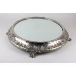 A Victorian silver plated table stand with circular mirrored top, sloping border decorated with