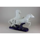 A Royal Dux porcelain ornament of two white leaping horses, on a dark blue base 30cm