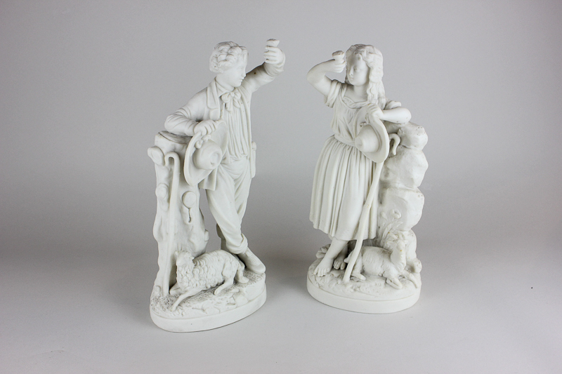 A pair of Parian figures of a shepherd and goatherd, the boy and girl both raising a flower and