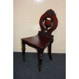 A mahogany hall chair with carved circular back and shield shaped central design on turned legs