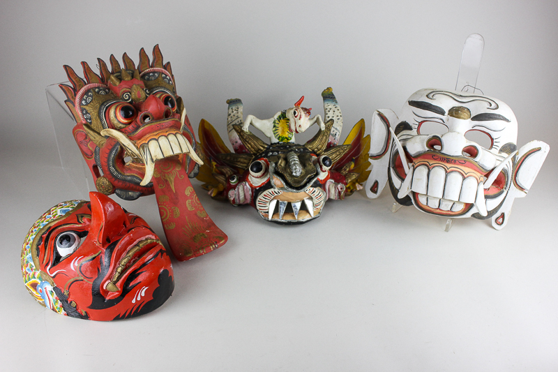 Four Balinese papier mache masks, all brightly decorated with fangs and pointed teeth