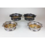 A set of four silver plated wine coasters with shell and scroll borders on turned wooden bases,