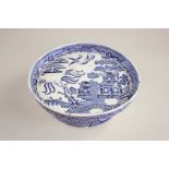 An English pottery blue and white willow pattern dish on stand, possibly an apprentice piece, 26cm