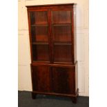 A mahogany bookcase with twin glazed doors enclosing two shelves above cupboard, on bracket feet,