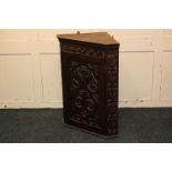 A carved corner wall cupboard with single panel door decorated with birds and scrolls, enclosing two