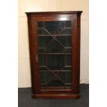 An oak corner cupboard with single glazed panel door enclosing three shelves, on shaped bracket