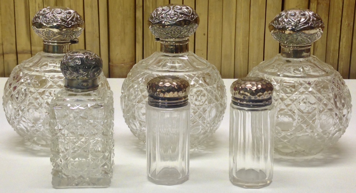 A SET OF THREE LARGE SPHERICAL CUT GLASS SCENT BOTTLES WITH SILVER TOPS ALONG WITH THREE OTHER