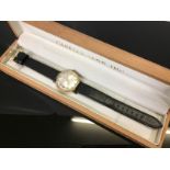 9CT GOLD GENTS GARRARD WRIST WATCH ON BLACK LEATHER STRAP SILVERED DIAL WITH GILT BATON MARKERS,