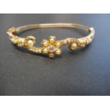 A yellow metal hinged bangle with diamond and seed pearls in floral setting, with safety chain,