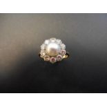 An 18ct gold and platinum ring with central pearl surrounded by ten diamonds in floral cluster