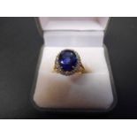 An 18ct gold ring with synthetic sapphire surrounded by sixteen diamonds in cluster setting - size