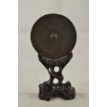 A miniature Chinese cast bronze mirror with scroll decoration - diam 12.5cm, on carved hardwood