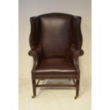 A late 19th/early 20th century Georgian style wing armchair upholstered in buttoned brown leather,