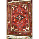 A Middle Eastern red ground rug with flowers and palmettes to centre, floral border - 103x74cm.