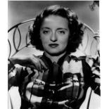 A BETTE DAVIS AUTOGRAPHED AND INSCRIBED BLACK AND WHITE PHOTOGRAPH, with Davis seated in a metal