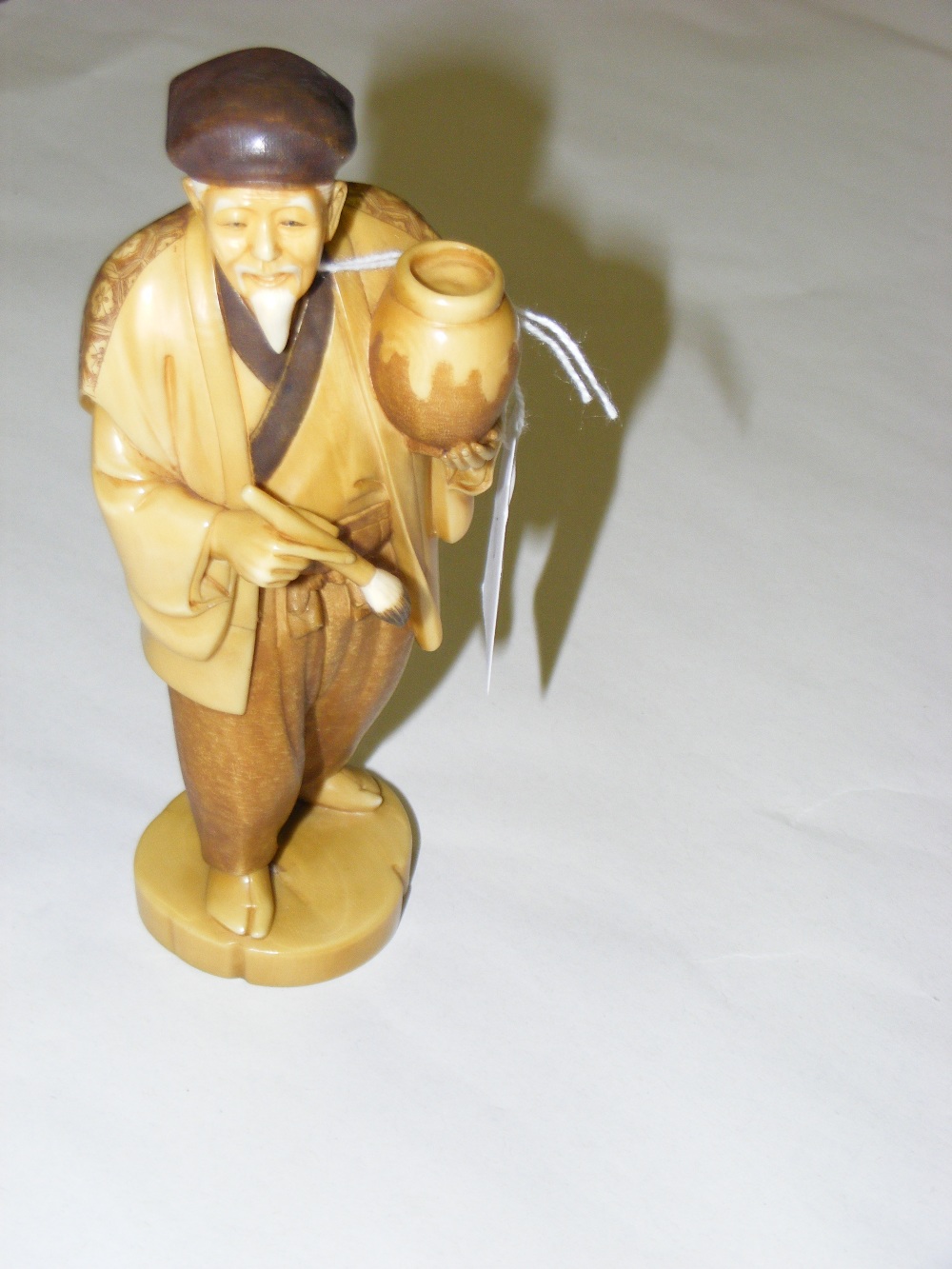 An early 20th century Japanese ivory okimono depicting a scholar with pot and brush in hand,