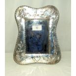 A 24cm x 20cm silver mounted photo frame with embossed cherub, flowers and foliage decoration