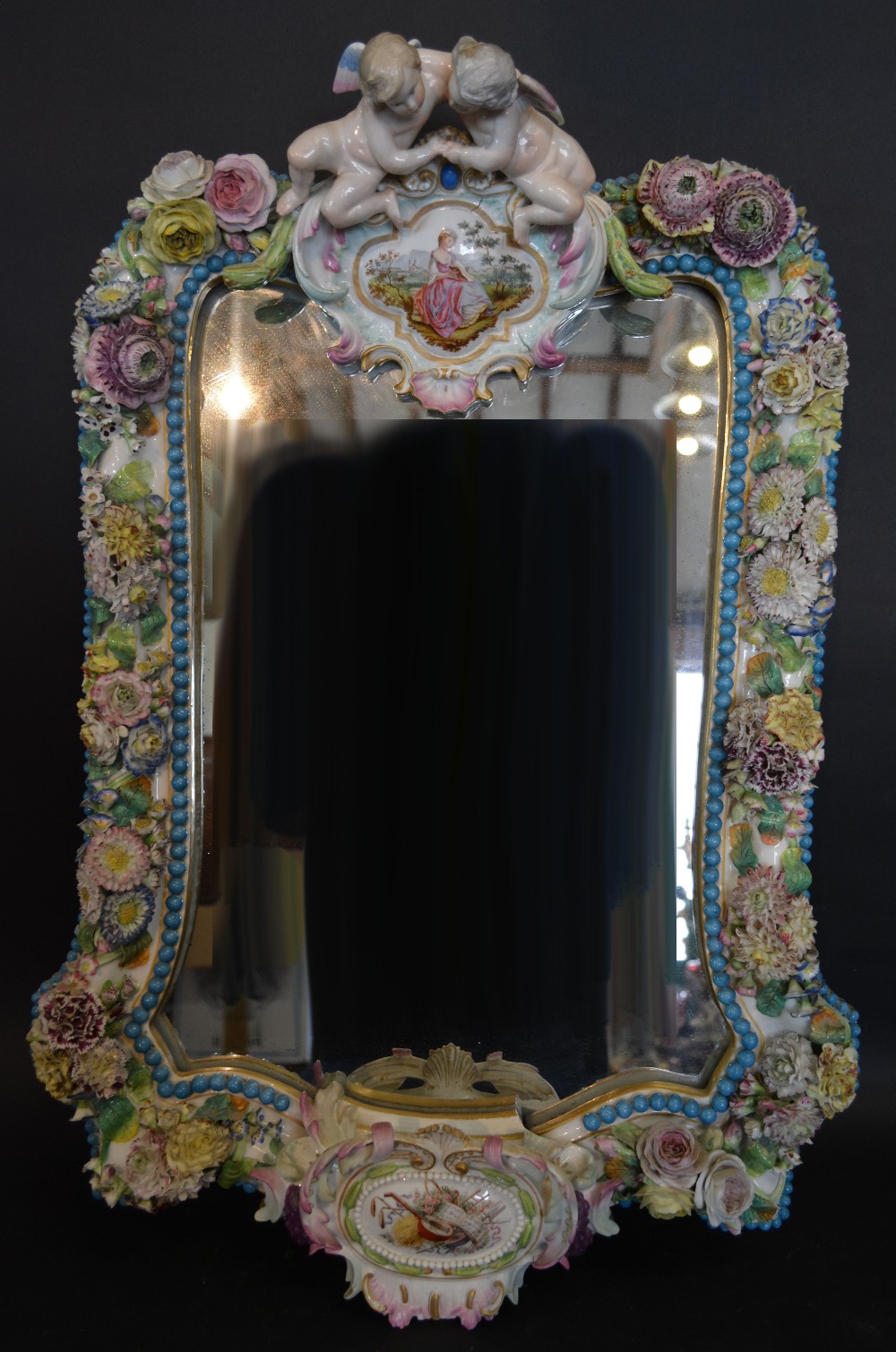 A Meissen Porcelain Large Wall Mirror with Putti Cresting above a cartouche hand painted with a
