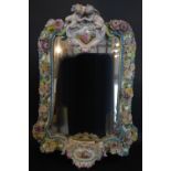 A Meissen Porcelain Large Wall Mirror with Putti Cresting above a cartouche hand painted with a