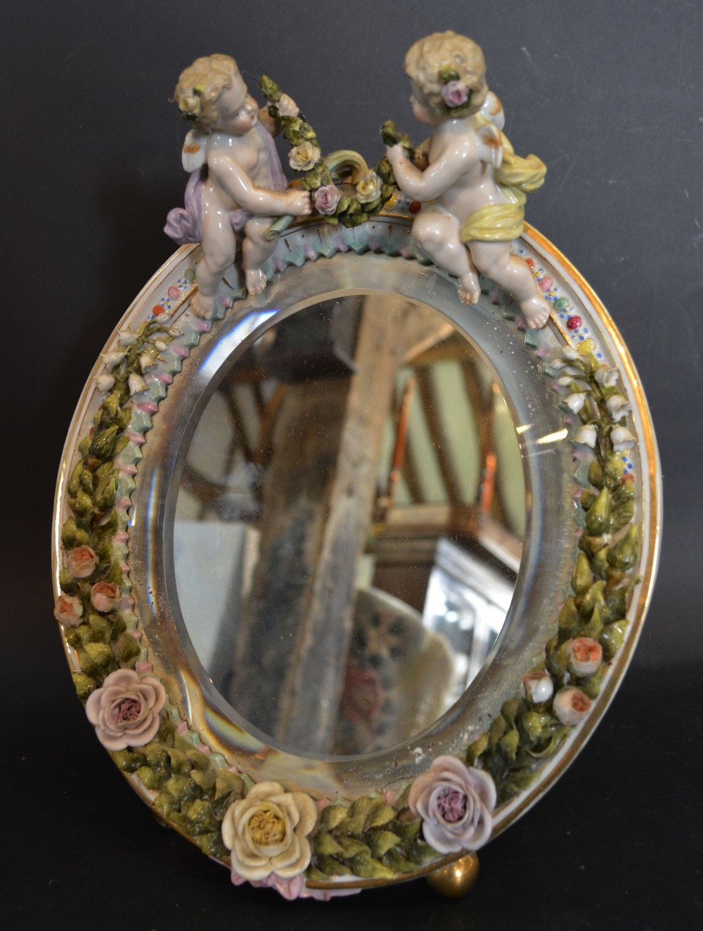 A Sitzendorf Porcelain Wall or Table Mirror of Oval Form with Putti Cresting,
