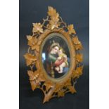 An Oval Painted Porcelain Panel Depicting Mother and Child within a Black Forest Carved Frame with