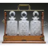 OAK CASED TANTALUS WITH THREE STOPPERED CUT GLASS DECANTERS. Handle marked "The Tantalus, London".