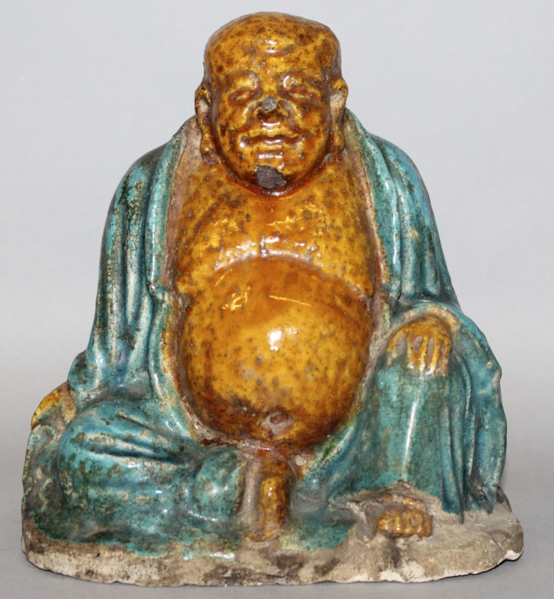 A 16TH CENTURY CHINESE MING DYNASTY FAHUA POTTERY FIGURE OF BUDAI, seated with exposed belly and one