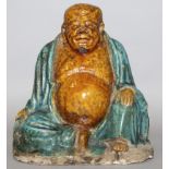 A 16TH CENTURY CHINESE MING DYNASTY FAHUA POTTERY FIGURE OF BUDAI, seated with exposed belly and one