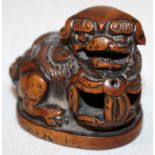 A JAPANESE CARVED WOOD NETSUKE OF A BUDDHISTIC LION, it's head resting on a pierced ribboned ball,